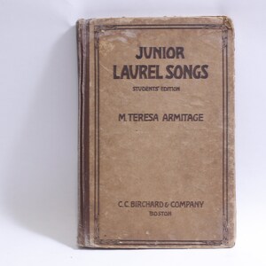 May include: A vintage book titled "Junior Laurel Songs" with the subtitle "Students Edition" by M. Teresa Armitage. The book is published by C.C. Birchard & Company in Boston.