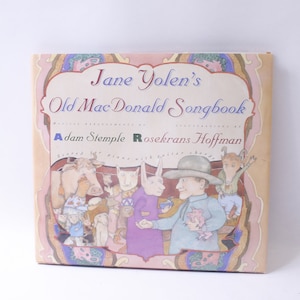 May include: A book cover with a pink background and a colorful illustration of a man and animals. The title is "Jane Yolen's Old Mac Donald Songbook" with the words "Music, arrangements, and illustrations by Adam Stemple Rosekrans Hoffman" underneath.