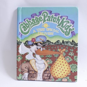 May include: A book cover featuring a cartoon stork wearing a pilot's uniform and carrying a baby in a yellow bag with red hearts. The book title is "Cabbage Patch Kids in A Very Special Delivery".
