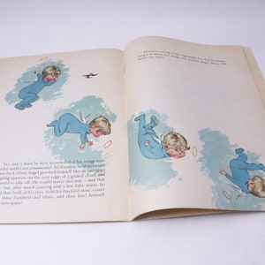 Pu&ograve; includere: Libro aperto con illustrazioni di un angioletto in pigiama blu con ali bianche, che cade nell'aria. Le illustrazioni sono in stile vintage, con testo sulle pagine.