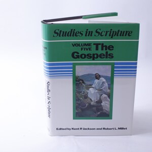 Può includere: Un libro con copertina rigida intitolato "Studies in Scripture, Volume Five: The Gospels". Il libro ha il dorso verde e la copertina bianca con un'illustrazione religiosa. È visibile anche il testo "Edited by Kent P Jackson and Robert L. Millet".
