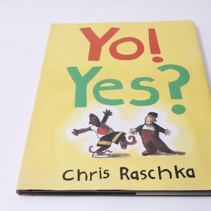 May include: A yellow book with the title "Yo! Yes?" in red and green letters. The book features an illustration of two people, one in red and black clothing and the other in brown and red clothing. The author's name, "Chris Raschka", is printed in black at the bottom of the cover.
