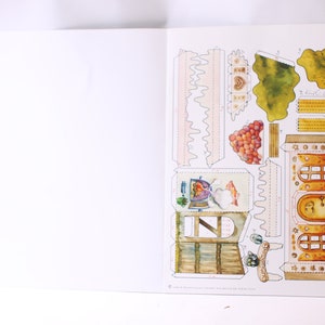 May include: A papercraft model kit featuring a detailed illustration of a whimsical house with a chimney, windows, and a door. The kit includes various pieces to assemble the house, including a roof, walls, and decorative elements. The house is surrounded by a green garden with trees and flowers.