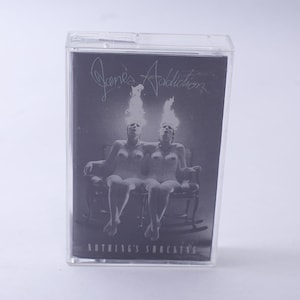 May include: A black and white cassette tape with the band name "Jane's Addiction" and the album title "Nothing's Shocking" printed on the front.