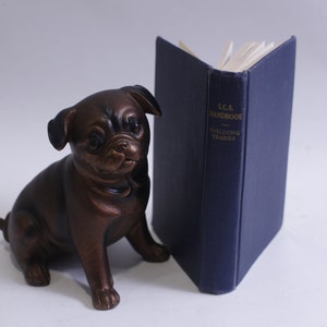 May include: A bronze pug figurine sitting next to a blue book titled "L.C.S. Handbook Building Trades".
