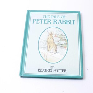 May include: A teal blue hardcover book with the title "The Tale of Peter Rabbit" and an illustration of a rabbit on the front cover. The book is by Beatrix Potter.