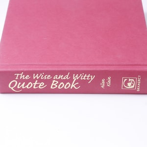 Könnte beinhalten: Ein rosafarbenes Hardcover-Buch mit dem Titel "The Wise and Witty Quote Book" von Allen Klein, herausgegeben von Gramercy.