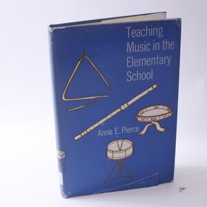 May include: A blue book titled "Teaching Music in the Elementary School" by Anne E. Pierce. The cover features illustrations of musical instruments, including a triangle, a flute, a tambourine, and a snare drum.