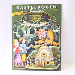 May include: A green and brown papercraft book with a 3D gingerbread house, a witch, and two children. The book is titled "Bastebogen Bastelspa&szlig;" and is a special edition for the 200th anniversary of the Brothers Grimm fairy tales. The book features the story of Hansel and Gretel.