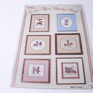 Peut inclure: Un livret de modèles de point de croix vintage intitulé "PAL Love Those Country Kids" avec six motifs différents représentant des enfants dans différentes scènes. Le livret est imprimé sur un fond blanc avec un motif de pois rose et blanc. Le prix est de 5,00 €.