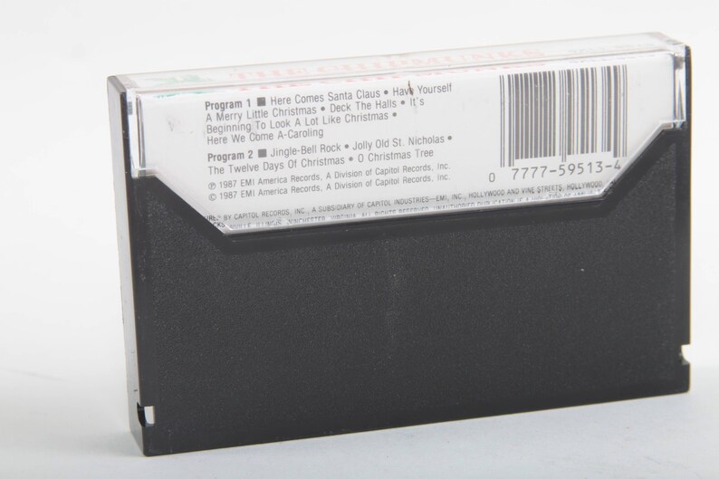 May include: A black cassette tape with a white label. The label lists the songs "Here Comes Santa Claus", "Have Yourself a Merry Little Christmas", "Deck the Halls", "It's Beginning to Look a Lot Like Christmas", "Here We Come A-Caroling", "Jingle Bell Rock", "Jolly Old St. Nicholas", "The Twelve Days of Christmas", and "O Christmas Tree". The label also includes the copyright information "1987 EMI America Records, A Division of Capitol Records, Inc.". The barcode is 0 7777-59513-4.