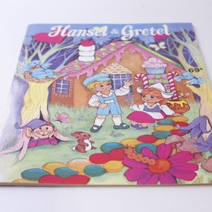 May include: A vintage children's book cover featuring Hansel and Gretel standing in front of a gingerbread house. The cover is illustrated with colorful candy and a candy cane path. The book title is "Hansel & Gretel" and the price is "69 cents".
