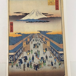 May include: A woodblock print depicting a bustling street scene in Japan. The print features a long, narrow street lined with shops and stalls. People are walking and shopping, and there is a mountain in the background. The print is titled "Mitsui's store / Prefectur" and is numbered "8".
