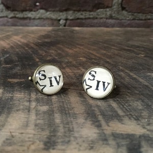 May include: A pair of gold cufflinks with a white background and black text that reads "S IV".