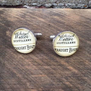 Pode incluir: Um par de botões de punho de prata com fundo branco e texto preto que diz "W.L. Weller Distillery Straight Bourbon".