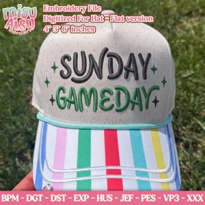 Op de afbeelding: Een witte baseballpet met een lichtroze stippenpatroon op de kroon en een meerkleurige verticaal gestreepte klep. De voorkant is voorzien van geborduurde tekst SUNDAY GAMEDAY in zwart en groen met kleine zwarte en groene steraccenten.