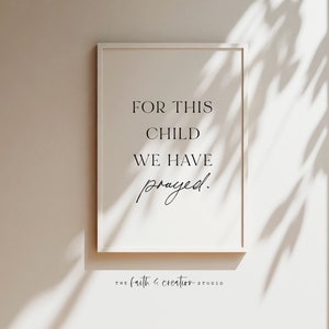 May include: A white framed print with the text "For this child we have prayed." The print is hanging on a beige wall with a shadow from a window.