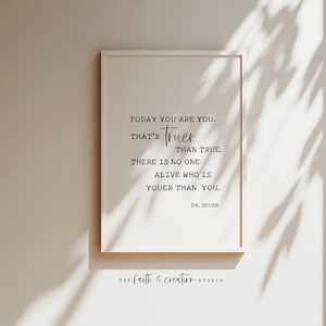 Può includere: Una stampa incorniciata bianca con una citazione in bianco e nero di Dr. Seuss che recita "Oggi sei te stesso. Questo è più vero del vero. Non c'è nessuno in vita che sia più te di te." La stampa è su una parete bianca con un'ombra da una finestra.