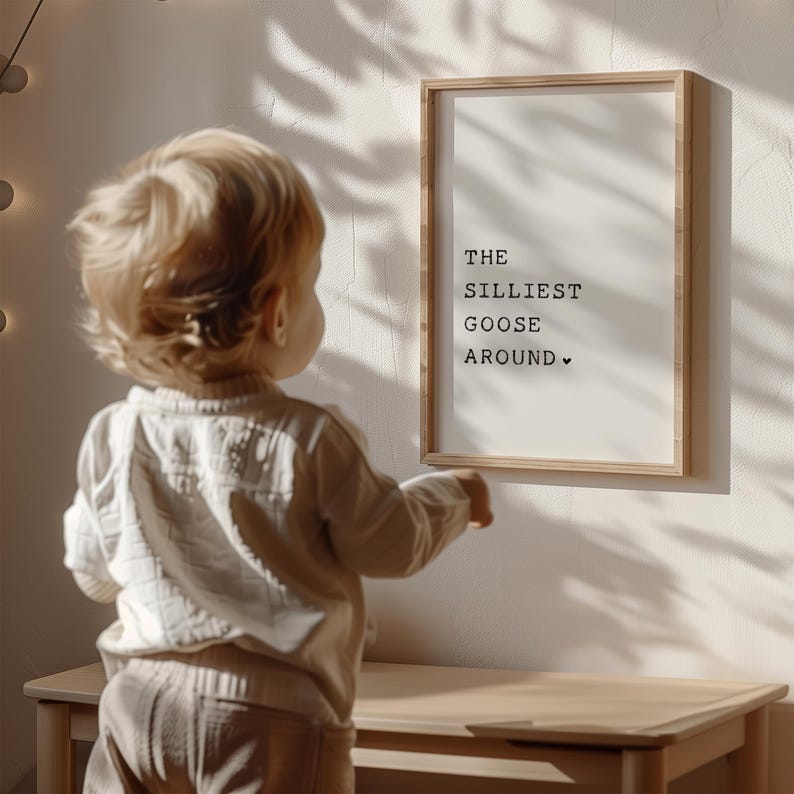 Pu&ograve; includere: Una stampa incorniciata con il testo "THE SILLIEST GOOSE AROUND" in lettere nere su sfondo bianco. Un bambino piccolo sta guardando la stampa.