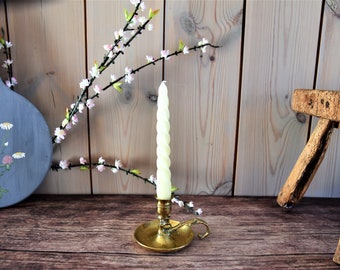 May include: A brass candlestick with a white candle on a wooden surface with a floral sprig in the background.