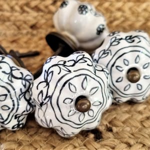 May include: Four white ceramic knobs with black floral designs. The knobs have a round shape and a small hole in the center for attaching to a drawer or cabinet.