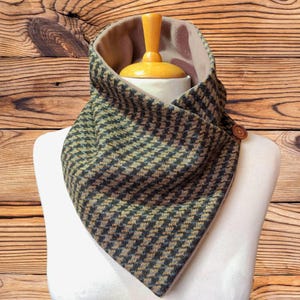 May include: A cowl neck scarf featuring a green, black, and brown houndstooth pattern on the exterior. The interior is lined with a solid light brown fabric. A single brown circular button is attached to the side of the folded fabric collar.
