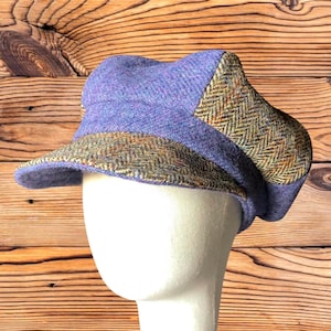 May include: A newsboy cap featuring a combination of solid lavender wool fabric and a contrasting olive green and brown herringbone tweed pattern on the brim and side panels. The hat has a structured crown and a short, stiffened visor brim.