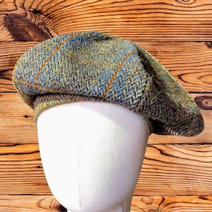 May include: A tweed beret featuring a textured weave in shades of olive green, brown, and grey, with subtle flecks of orange and blue throughout the fabric. The hat has a rounded, soft crown and a structured band that sits securely on the head.