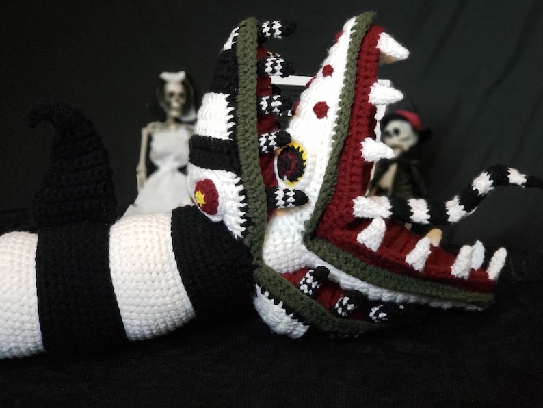 Puede incluir: Un juguete de peluche de ganchillo de una criatura con rayas blancas y negras con una gran boca abierta. La boca de la criatura es roja y verde con dientes blancos. El juguete est&aacute; posado como si fuera a tragar algo.