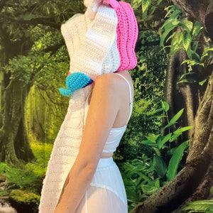 May include: A handmade crochet unicorn hat with a long white scarf, pink horn and ear details, and a blue and pink accent. The hat is part of a costume or accessory set.