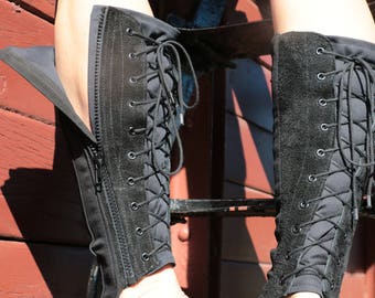 May include: A pair of black leather boots with laces and a zipper up the back. The boots are open at the heel and have a strap around the ankle.