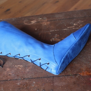 May include: A blue leather boot with black laces. The boot is laced up the side and has a pointed toe.
