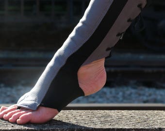 May include: A gray and black leather foot and ankle protector. The protector has a gray leather panel on the front, black side panels, and a lace-up closure on the back. The foot is exposed.