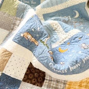May include: A patchwork quilt featuring blue, green, and brown fabric squares with patterns including dots, plaids, and florals. The blue sections display illustrations of rabbits, moons, and stars with the text "I Love You" and "Guess how much".