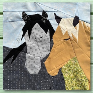May include: A patchwork quilt block featuring two horse heads, one gray and one brown, against a blue background. The quilt block is made of various fabric scraps and is a great example of a modern quilting technique.