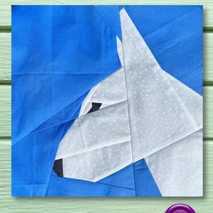 May include: A white and blue fabric patchwork design of a dog's head. The dog's head is facing the left side of the image. The background is blue and the dog's head is white with black accents.