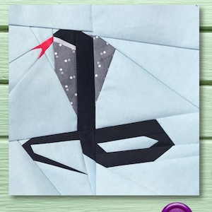 Puede incluir: Un cuadrado de tela azul claro con un diseño geométrico en blanco y negro. El diseño es una serpiente estilizada con una lengua roja.