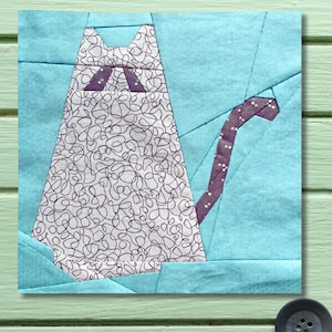 May include: A fabric cat design in a patchwork style. The cat's body is white with a black squiggly pattern, and the tail is purple with white dots. The background is light blue, and the design is on a square piece of fabric.