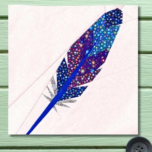 May include: A colorful, geometric feather design. The feather features a vibrant blue stem and is filled with floral patterns in shades of purple, blue, and pink. The background is a soft pink, with subtle geometric lines.