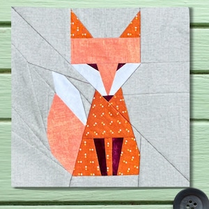 May include: A square fabric block featuring a geometric fox design. The fox is composed of orange, white, and burgundy fabric pieces, with a dotted pattern on the body. The background is a light gray fabric, and the overall style is reminiscent of quilting or patchwork.