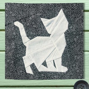 May include: A white paper origami cat on a black background with a white squiggly pattern.