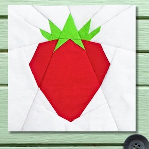 Peut inclure: Un bloc de tissu carré avec un motif géométrique de fraise rouge et de feuilles vertes. La fraise est centrée sur un fond blanc, composé de divers morceaux de tissu. Le bloc est probablement destiné au quilting ou à l'artisanat, avec des mesures en cm.