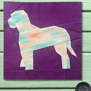 May include: A fabric square featuring a geometric dog design. The dog is constructed from light blue, peach, and white patterned fabric, set against a purple polka-dot background. The square is a patchwork design, suitable for quilting or crafting.