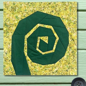 May include: A square fabric block featuring a geometric design. The central element is a dark green spiral, surrounded by a yellow and green patterned background. The design is reminiscent of a stylized flower or plant form. The block is likely part of a larger quilt or textile project.