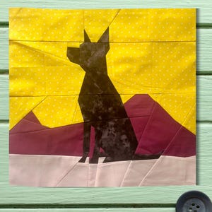 May include: A black paper silhouette of a dog sitting on a pink, white, and burgundy background. The background is a yellow fabric with white polka dots.