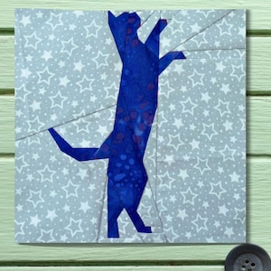 Peut inclure: Silhouette d'un chat bleu sur une pièce de tissu. Le chat bleu vif présente un motif marbré, sur un fond gris avec des étoiles blanches. L'œuvre d'art est carrée et semble être un bloc de courtepointe.
