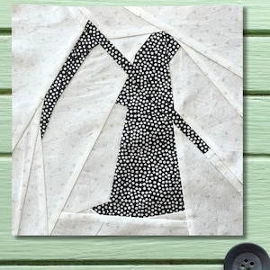 May include: A fabric quilt block depicting a Grim Reaper in black and white. The Reaper's robe and scythe are black with white polka dots, set against a white and light grey background. The block is square and appears to be handmade.