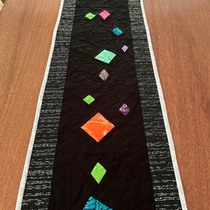 Puede incluir: Un camino de mesa negro con un borde blanco y una fila de parches de tela de forma de diamante de colores en el centro.