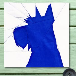 May include: A square fabric quilt block featuring a geometric, paper-pieced design of a Scottish Terrier dog head. The dog is constructed from solid royal blue fabric pieces set against a stark white background, creating sharp, angular lines.