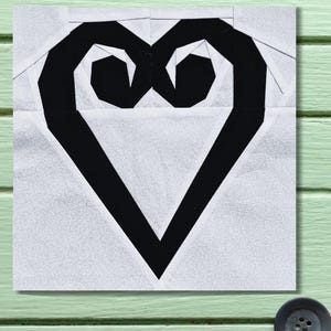 May include: A black and white fabric heart design. The heart is a bold black shape with a geometric design, set against a white background with a subtle, patterned texture. The heart's shape is a stylized representation, perfect for quilting or fabric crafts.